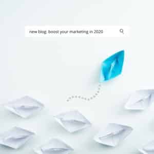 google search bar with the search term 'boost your marketing in 2020' above a collection of white paper boats. One blue boat is veering to a new direction